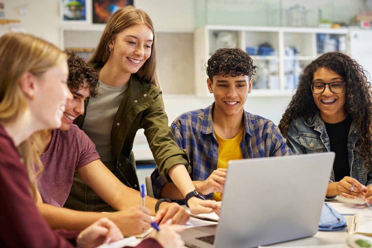 Diverse teens collaborating around a laptop during a digital study session, pointing at the screen and sharing ideas